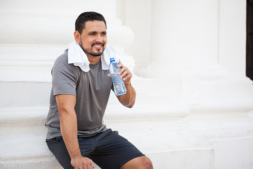 Portrait of a handsome young man working out in the city and taking a break to drink some water and rest