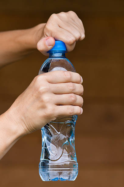 hands opening bottle with water hands opening bottle with fresh water on blurred background opening bottle cap photos stock pictures, royalty-free photos & images