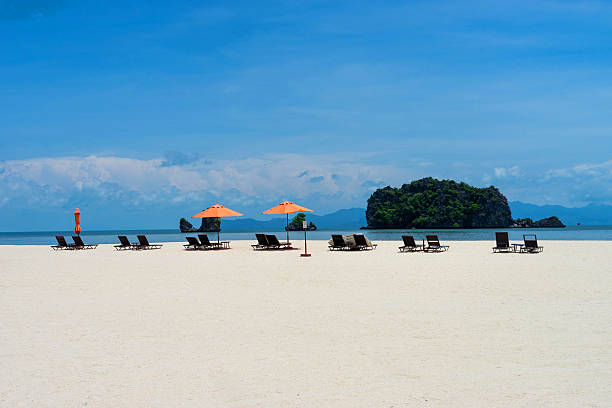 Tropical island scene with blue skies and white sandy beaches. Sunbeds and umbrellas overlook the ocean, a paradise view from Langkawi Island, Malaysia. Holiday photograph.