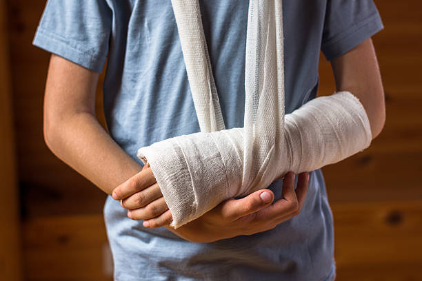 Boy with arm in plaster indoors on the brown background Boy with an arm in plaster indoors on the brown background , careless behavior at home, being in hospital, injury and health concept plaster stock pictures, royalty-free photos & images