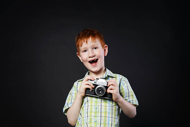 il bambino scatta foto con una fotocamera vintage su sfondo nero - fashionable studio shot indoors lifestyles foto e immagini stock