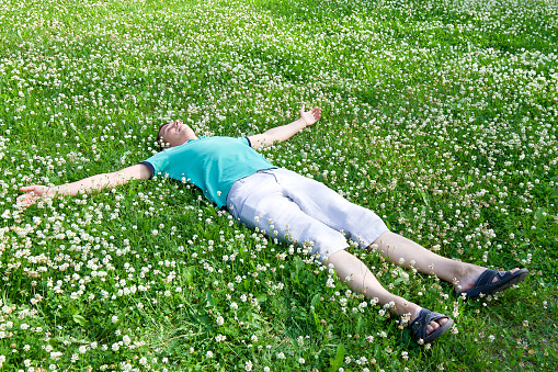Happy man lying arms outstretched on a green summer meadow among wildflowers