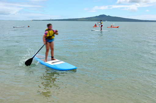 Auckland, New Zealand - January 11, 2016: People row on stand up paddle boards (SUP) in mission bay in Auckland New Zealand. It's an emerging global sport with a Hawaiian heritage. It's an ancient form of surfing for longer distances.