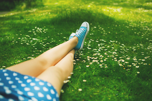 Unrecognizable female person relaxing on a green grass, enjoying a carefree summer day in the nature.