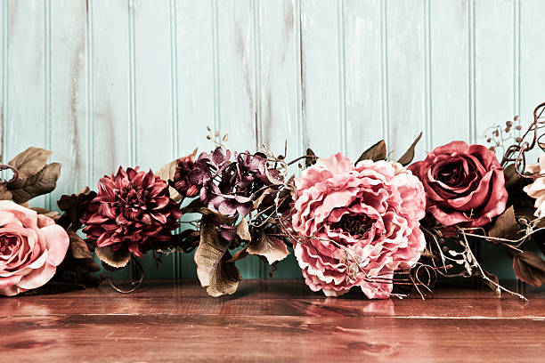 Dried floral arrangement in pink and brown hues.  The flowers lie at top of a wooden table with light blue background.  Copyspace.