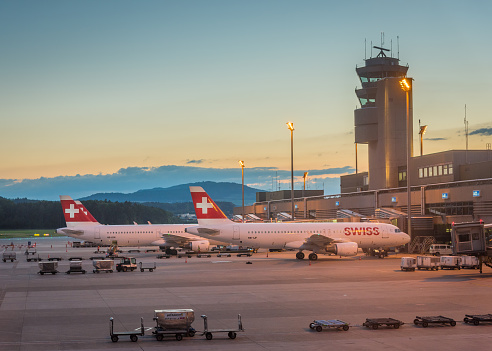 Zurich, Switzerland - July 6, 2016: Kloten airport in Zurich featuring control tower and Swiss International Air Lines aircrafts parked at the gates. The image was taken just after sunset. 