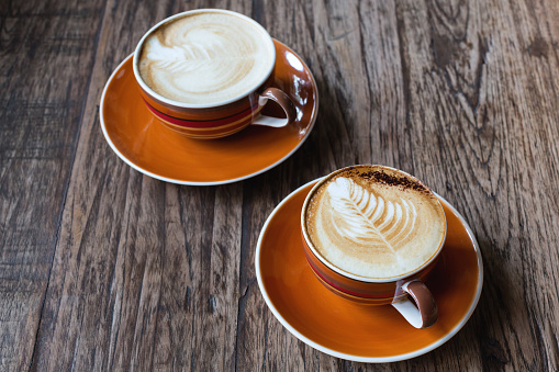 Two hot latte in a orange ceramic cup  on wooden table.