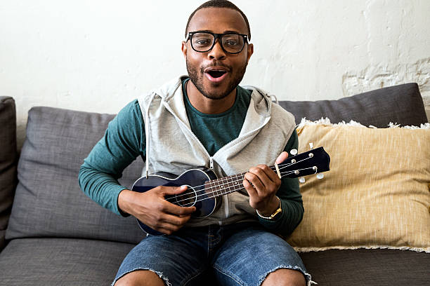 schöne junge schwarze mann spielt die gitarre zu hause. - ukulele stock-fotos und bilder
