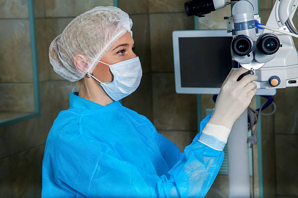doctor in breathing mask cheks surgical microscop in operation room - microscop imagens e fotografias de stock