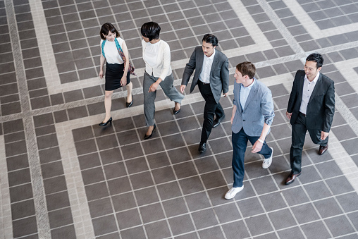 Multiracial group of business people walking and talking together in a modern office building foyer. View from elevated position.