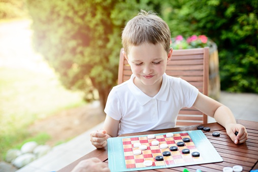 Little boy playing checkers board game on the terrace