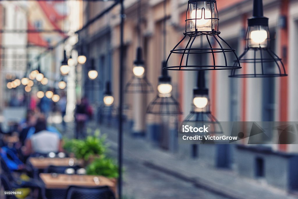 Lamps beautiful design in a restaurant on a street Beautiful design lamps over the tables of the restaurant on a stone street in the evening the old town of Riga. Blurry Abstract Stock Photo