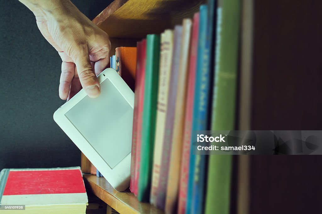 man hand gets ebook among old books from the bookshelf mans hand gets ebook among old paper books from the bookshelf. new technology concept E-Reader Stock Photo