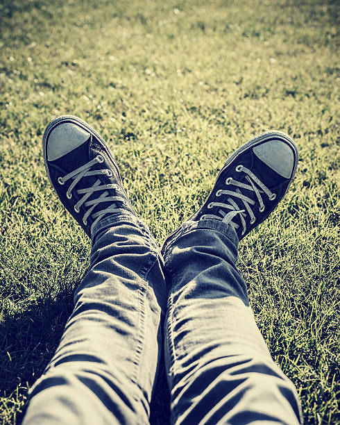 Closeup photo of lazy teen guy lying down on green grass an wearing stylish trendy gumshoes, body part, relaxing outdoors, sportive shoes, fashion for hipster