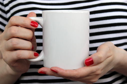 Girl is holding white cup, mug in hands. Mockup for designs.