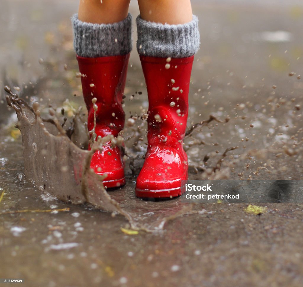 Child wearing red rain boots jumping into a puddle Child wearing red rain boots jumping into a puddle. Close up Puddle Stock Photo