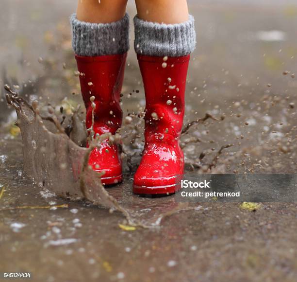 Child Wearing Red Rain Boots Jumping Into A Puddle Stock Photo - Download Image Now - Puddle, Jumping, Red