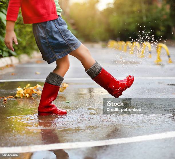 Child Wearing Red Rain Boots Jumping Into A Puddle Stock Photo - Download Image Now - Jumping, Asphalt, Child