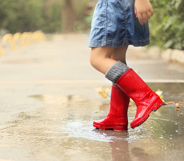 istock Child wearing red rain boots jumping into a puddle 545124552