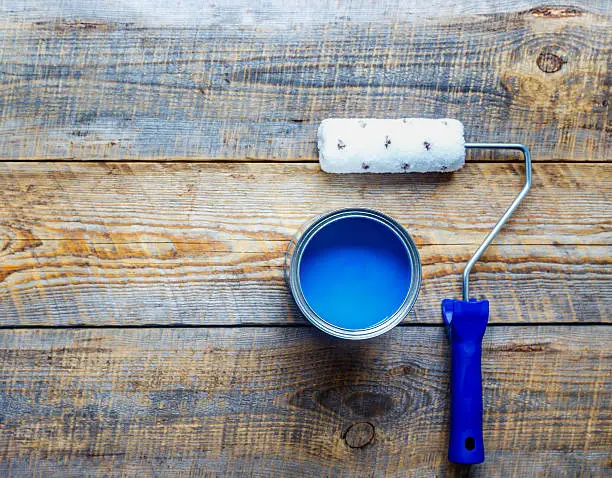 painting with can of blue paint and roller top view on wooden background