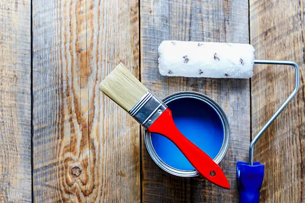 preparation for painting with can of blue paint and red brush with paint roller top view