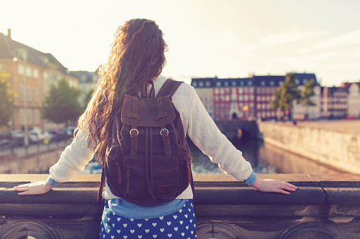 Unrecognizable female person with a backpack on her shoulders standing on the bridge and looking at the cityscape of Copenhagen.