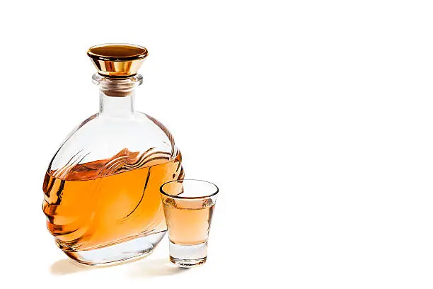 Bottle and a shot glass of tequila on a white background