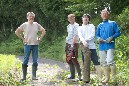 Kyoto iStockalypse.  A group of male neighbours in a small village community rest after helping each other clear a fallen tree from a road in rural Nara, Japan using a chainsaw and knife.