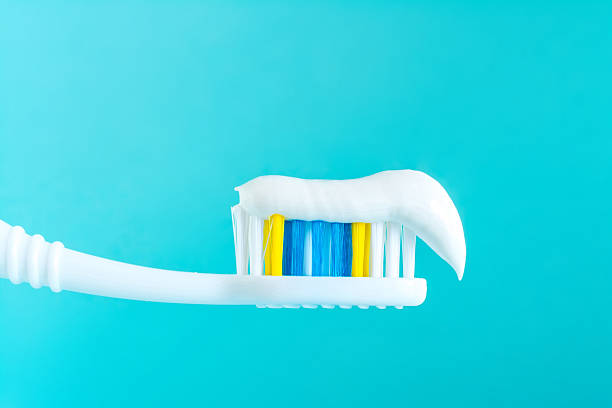 dentifricio su uno spazzolino da denti da vicino su sfondo blu - toothpaste glue blue white foto e immagini stock