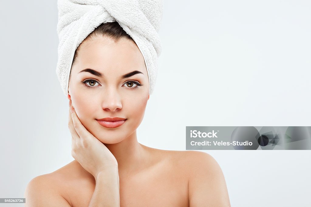 Young girl wearing white rowel at gray studio background Young girl with big eyes and dark eyebrows, wearing white towel on head and with naked shoulders, holding hand with nude nails near face, light nude make-up, gray studio background, beauty photo Towel Stock Photo