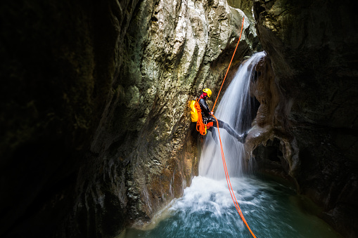 Canyoneering member with backpack rappeling down the small waterfall in the canyon.