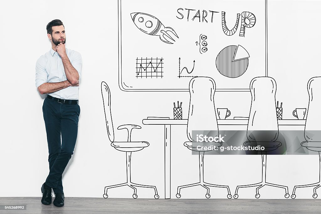 Dreaming about new business. Handsome young man in smart casual wear standing in front of the wall and near the pencil drawn office interior Day Dreaming Stock Photo