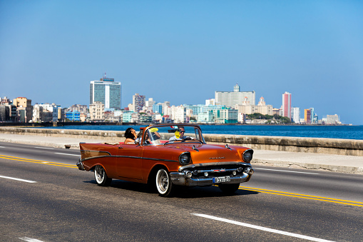 Havana, Сuba - April 16, 2016: Vintage American car with tourists speeding along the Malecon in Havana, Cuba, motion blur, skyline of modern Havana with hotels in Vedado is visible in the background, 50 megapixel image.