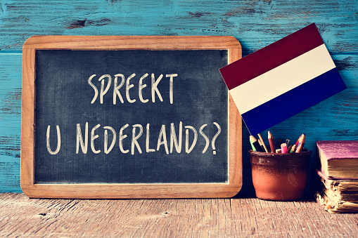 a chalkboard with the question Spreekt u Nederlands?, do you speak Dutch? written in Dutch, a pot with pencils, some books and the flag of the Netherlands on a wooden desk