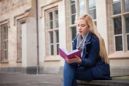 A blonde, female student sits alone and reads. University / college setting with copyspace.