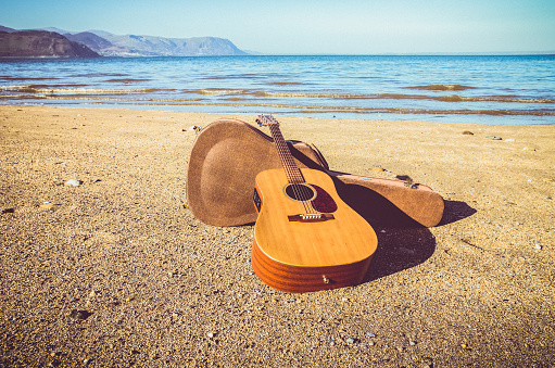 Acoustic guitar on a deserted beach with blue sky and sea.