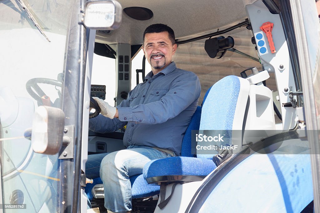 Cheerful driver sitting in big field engine Cheerful driver sitting in big field engine on farm Leaning Stock Photo
