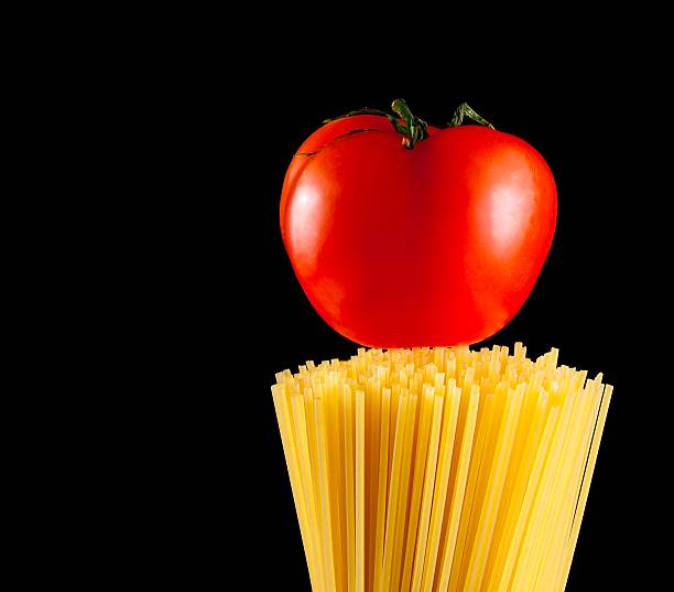 raw pasta spaghetti with tomato on top on black background