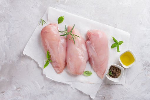 Raw chicken breast with rosemary, olive oil  and peppercorns, selective focus. Culinary cooking ingredients