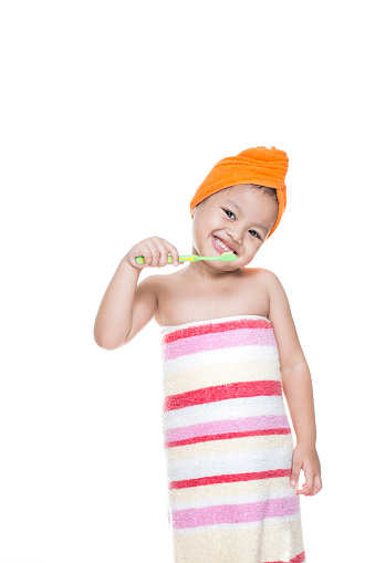little girl brushing teeth with a smile, wearing a towel, and towel on head