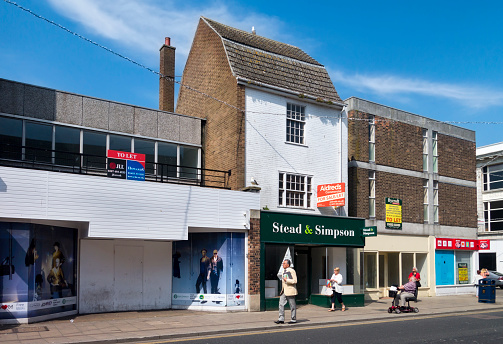 Great Yarmouth, Norfolk, England - June 8, 2016: A few people passing a row of empty shops in King Street, in Great Yarmouth, Norfolk, eastern England, on a sunny spring day. Great Yarmouth’s fortunes have deteriorated over recent decades and many shops have closed. The tourist industry has also declined, as well as its fishing and North Sea gas and oil industries.