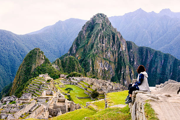 Woman overlooking the Inca ruins of Machu Picchu Woman sitting on a ledge and overlooking the Inca ruins of the city of Machu Picchu seen in the background. machu picchu photos stock pictures, royalty-free photos & images