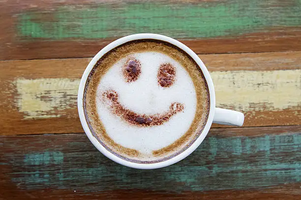 Photo of Smile face drawing on latte art coffee , wood color background