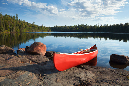 Red canoe on rocky shore of calm northern lake