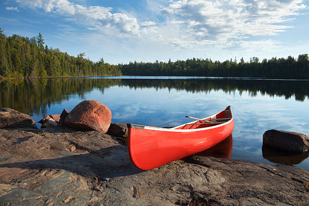 Red canoe on rocky shore of calm northern lake stock photo