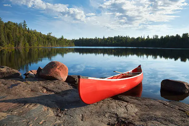 Photo of Red canoe on rocky shore of calm northern lake