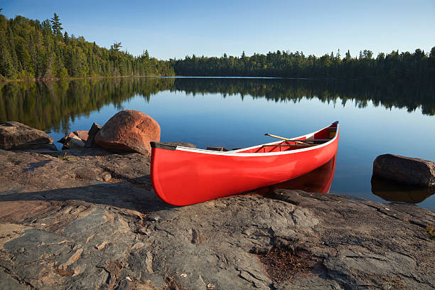 canoa roja en la orilla rocosa del lago tranquilo del norte - canoeing canoe minnesota lake fotografías e imágenes de stock