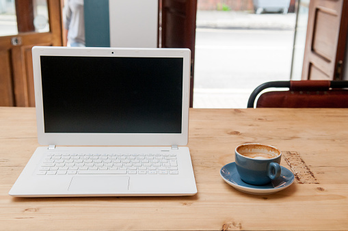Fresh cup of coffee and laptop computer on a wooden table background in the cafe