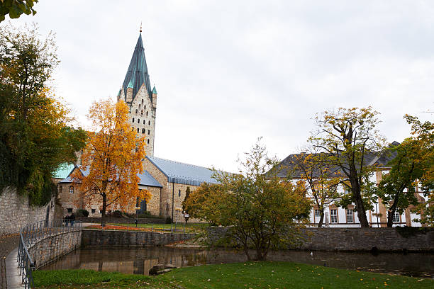 Paderborn, Germany - October 26, 2012: Cathedral Paderborner Dom seen from Paderquellen in autumn. Some people are walking on pathway around river.