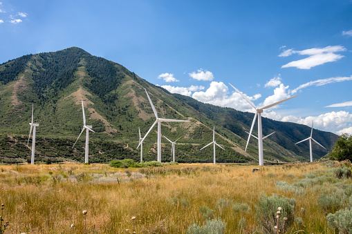 A cluster of wind turbines located at the bottom of a foothill in a high desert location.